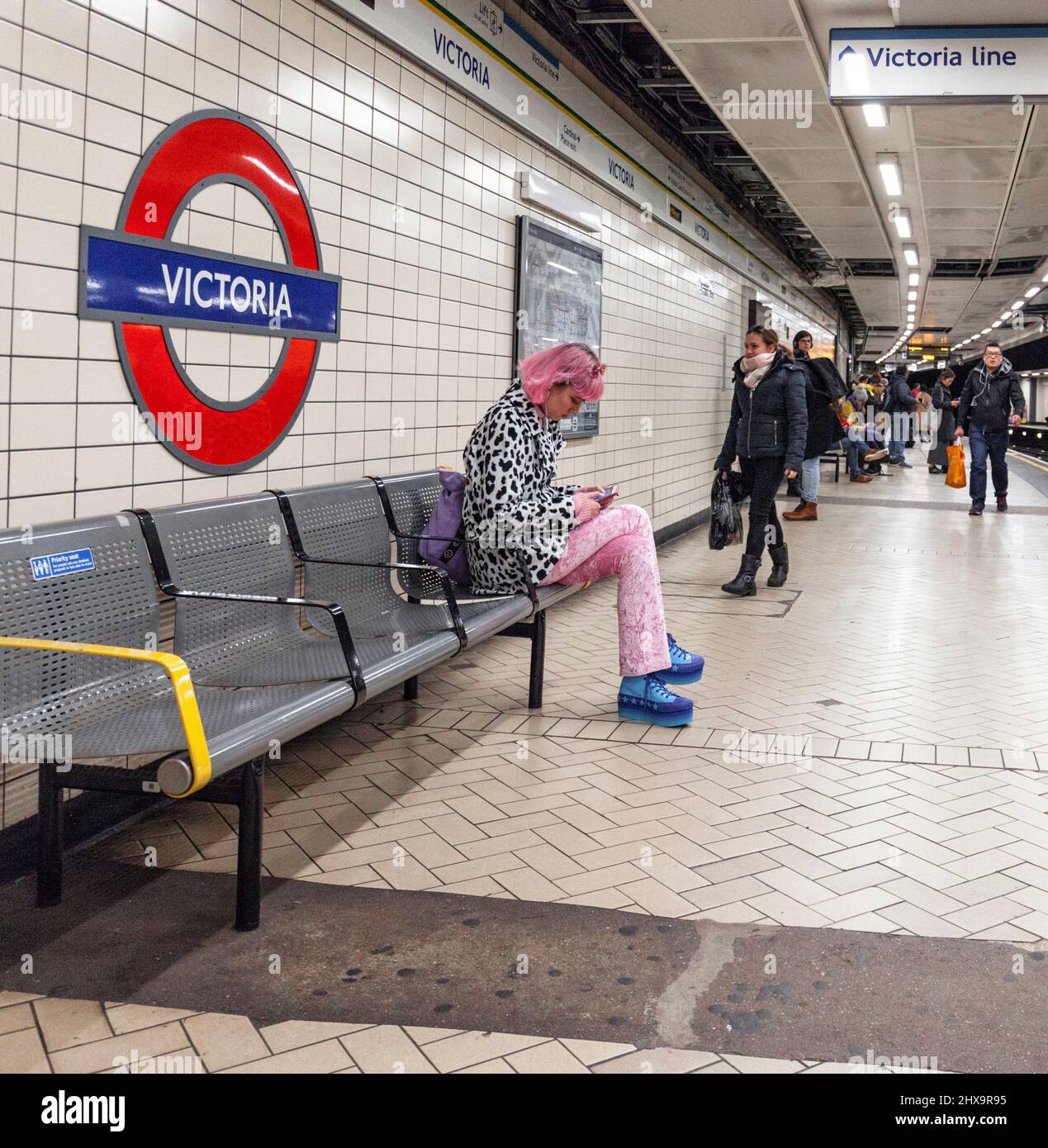London Victoria Victoria line London underground platforms with waiting tube passengers including on on a bench in front of the Underground roundel Stock Photo