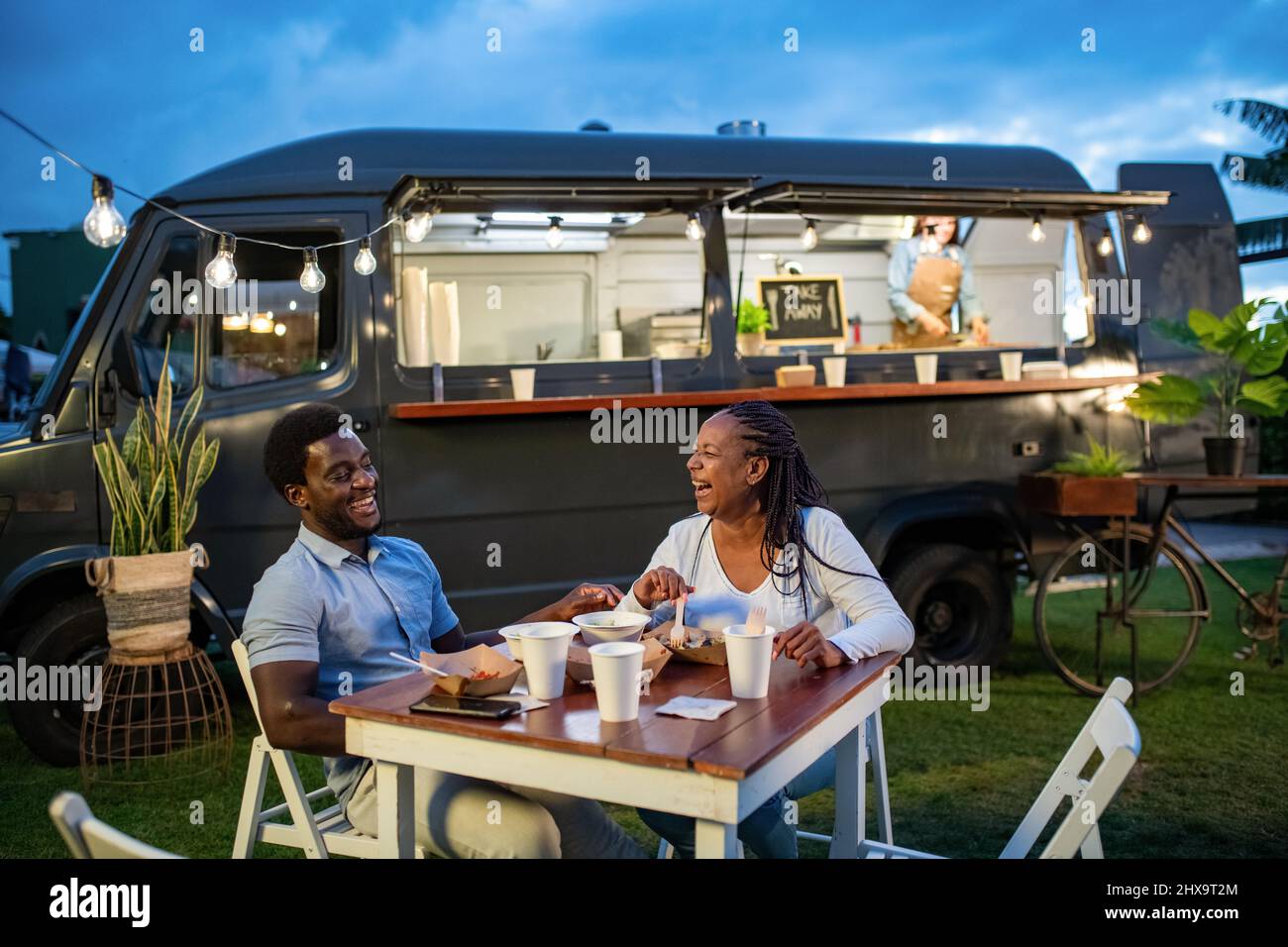 Happy black couple eating near food truck in evening Stock Photo