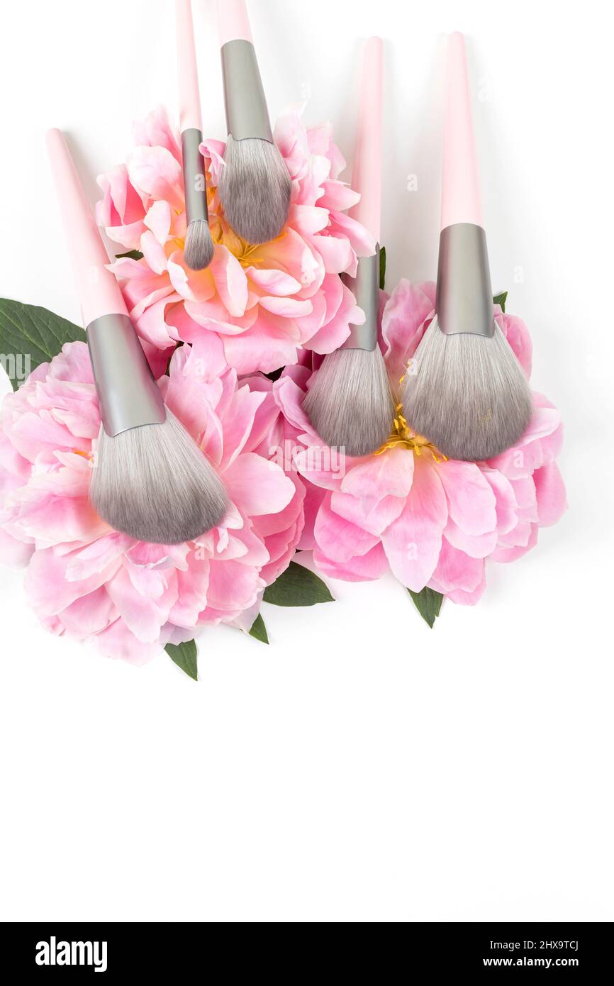 Different makeup brushes with pink peonies flowers on white background. Professional cosmetic makeup set. Accessories for beauty. Stock Photo