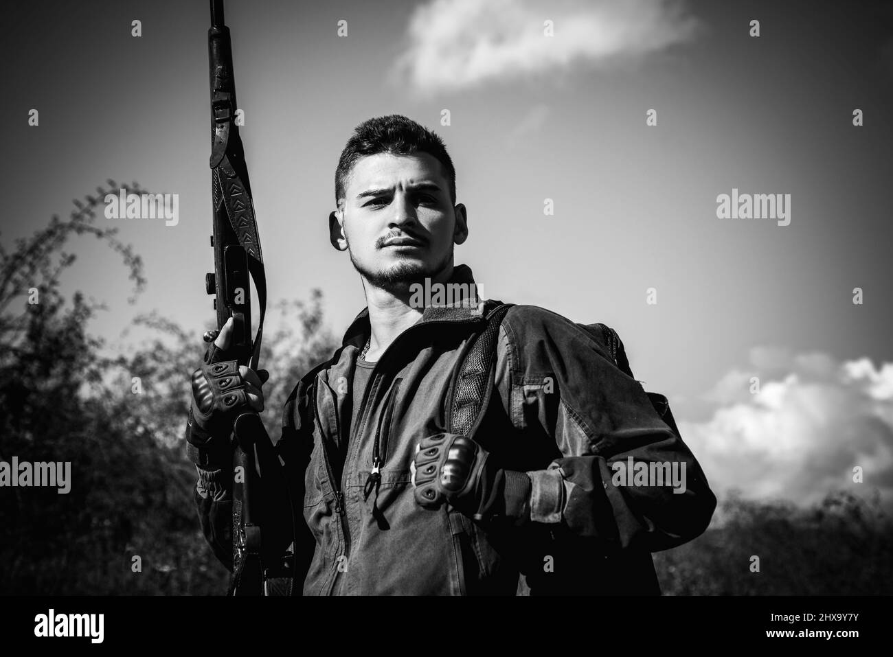 Close up Portrait of hamdsome Hunter. Poacher with Rifle Spotting Some Deers. Illegal Hunting Poacher in the Forest. Hunter with shotgun gun on hunt. Stock Photo