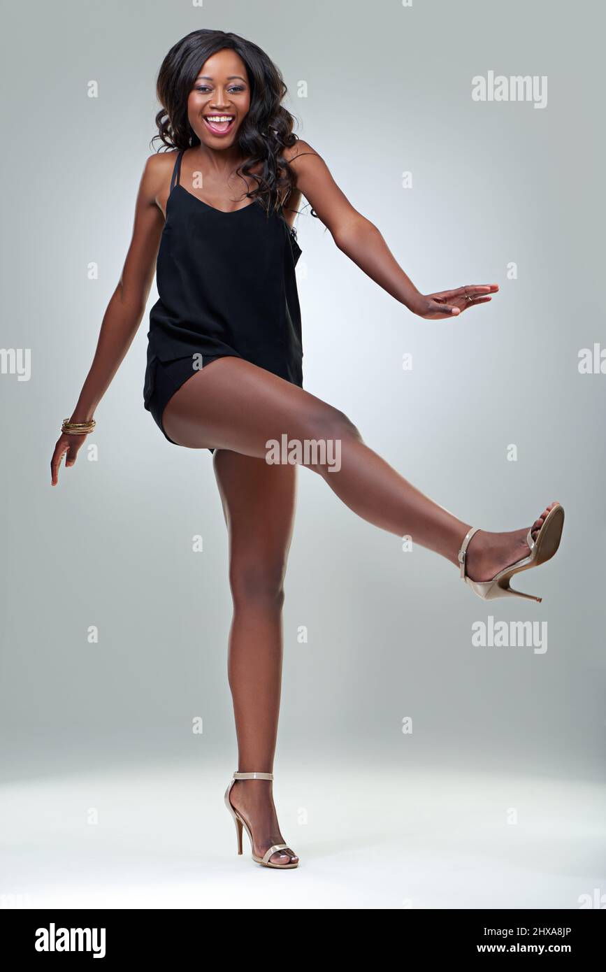 Fashionably fun. Studio shot of a beautiful young woman posing in a black dress against a gray background. Stock Photo