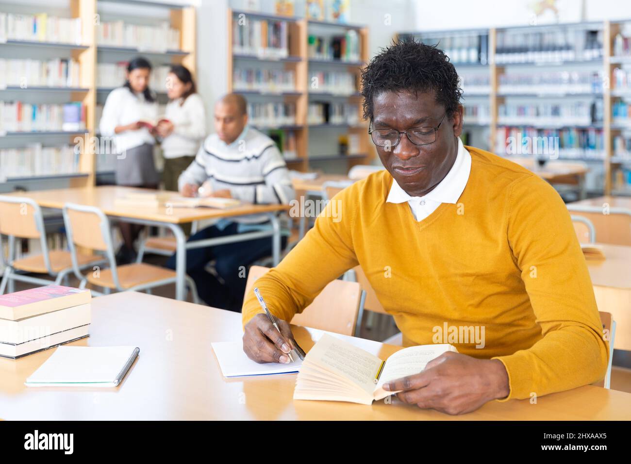 Focused adult African American reading books in public library Stock