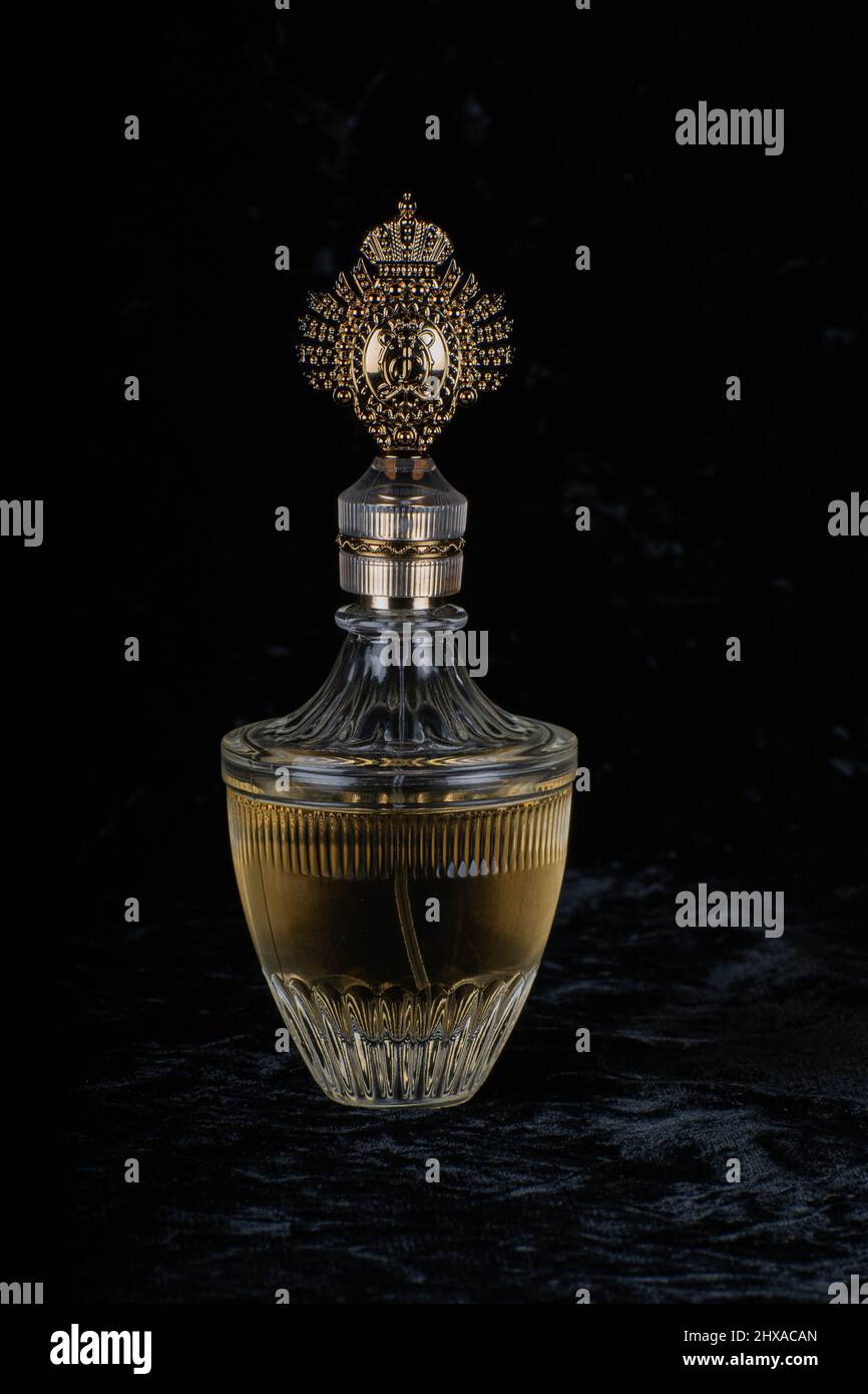 A golden transparent perfume bottle with drops on a wet pebble beach.  Close-up. In the background, the sea surf is blurred. Perfume advertising  concept Stock Photo