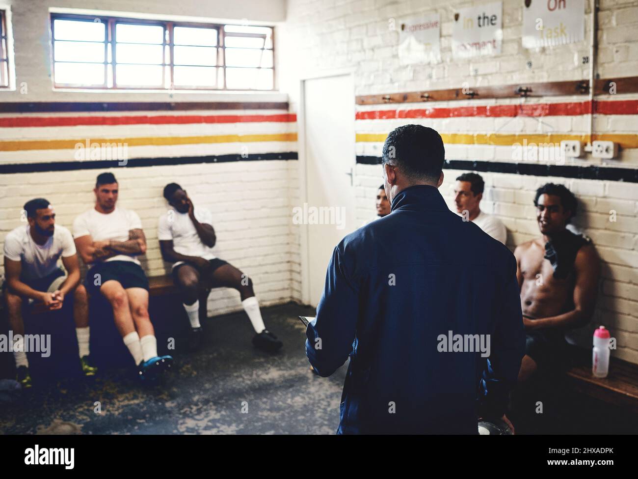 So heres what were going to do.... Cropped shot of a rugby coach addressing his team players in a locker room during the day. Stock Photo