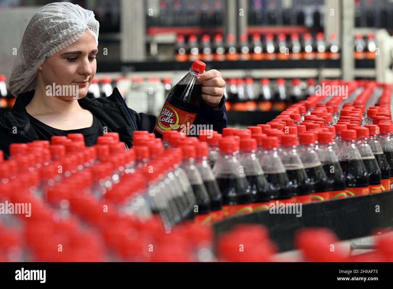 Schmalkalden, Germany. 07th Mar, 2022. Kaja Müller, an employee of Thüringer Waldquell Mineralbrunnen GmbH, stands at the production line during the filling of Vita-Cola. Thüringer Waldquell Mineralbrunnen GmbH, based in Schmalkalden, is a subsidiary of the Hassia Group. It employs 153 people including 8 trainees. The company bottles soft drinks under the three brands Thüringer Waldquell, Rennsteig and Vita Cola. Credit: Martin Schutt/dpa-Zentralbild/dpa/Alamy Live News Stock Photo