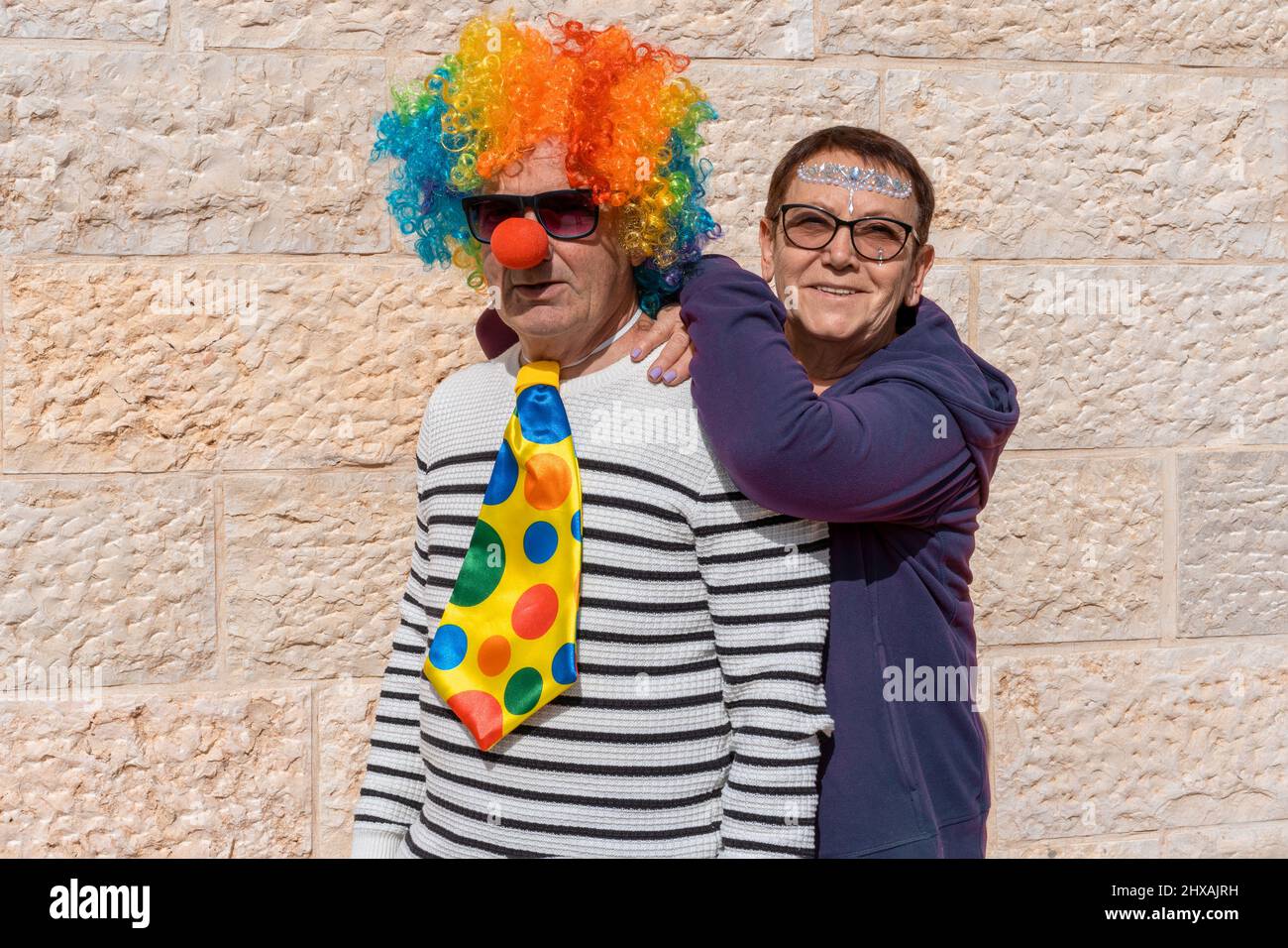Funny senior couple dressed up for Halloween or Purim or birthday party.  Funny old man in a clown costume and happy senior woman with face stickers  celebration Purim Jewish Holiday Stock Photo -