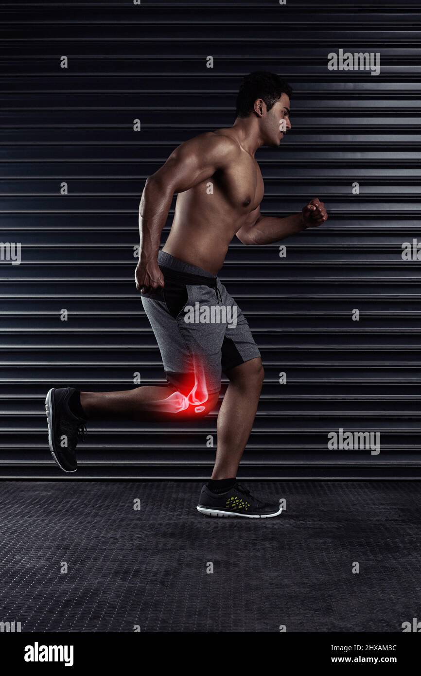 Feeling the pressure on his knee. Full length shot of a handsome young man running against a dark background. Stock Photo