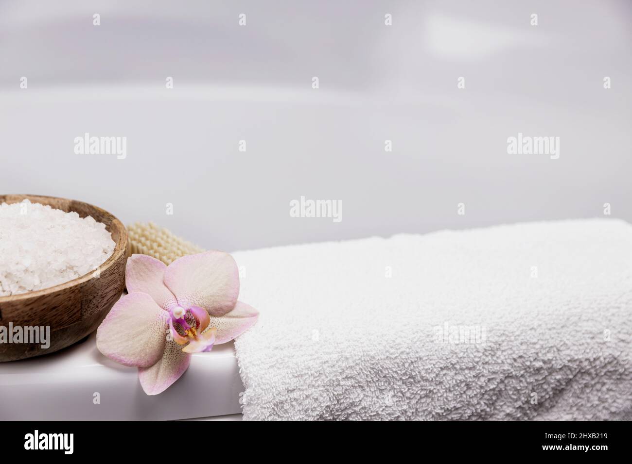 Preparation for hotel spa treatment, home bath procedure. White washbasin in bathroom, accessories on tray. Foot or body brush, white towel, sea salt in bamboo bowl, orchid flower. High quality photo Stock Photo