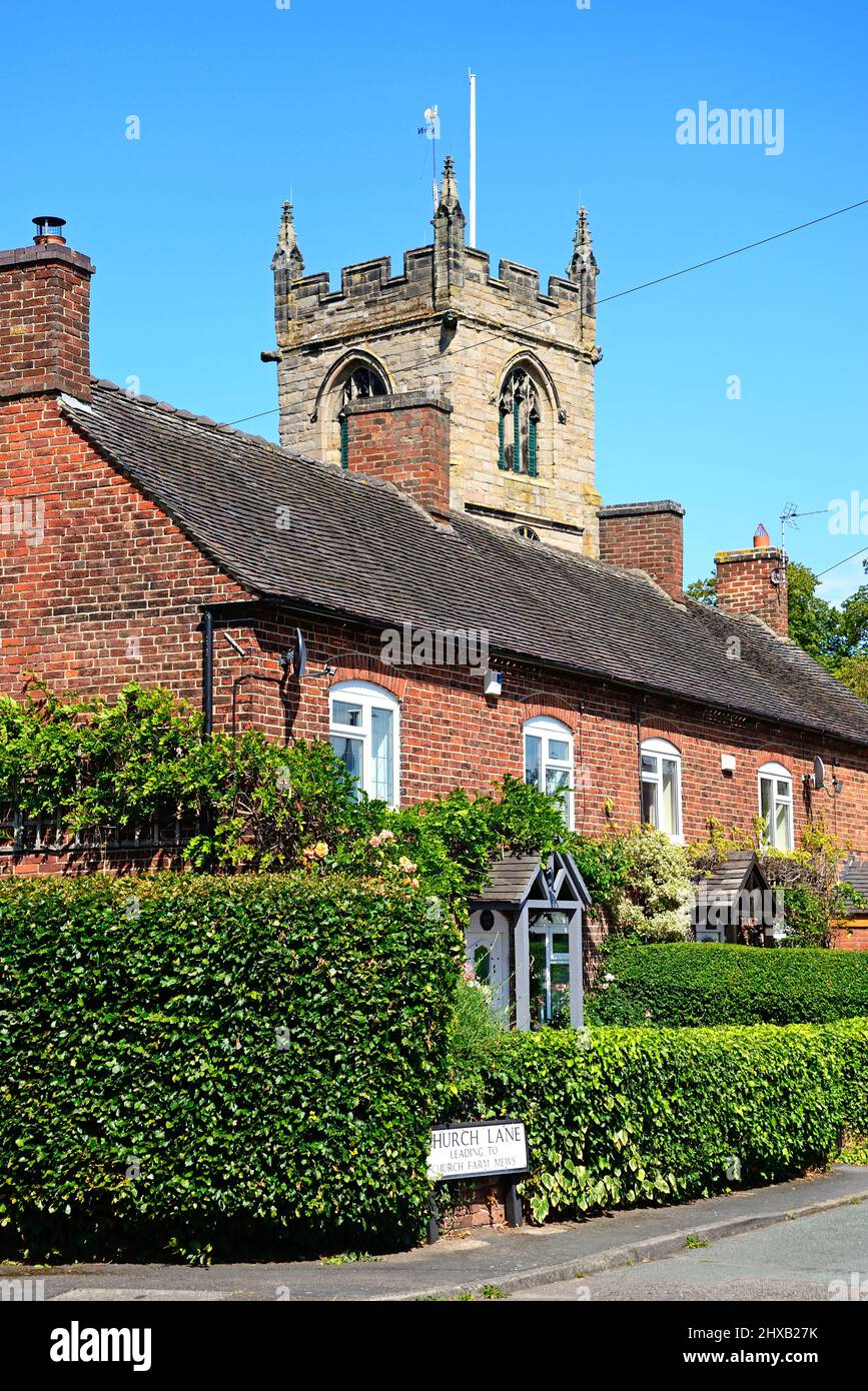 Row of traditional red brick building with All Saints Church to the rear along Church Lane, Kings Bromley, Staffordshire, England, UK, Europe. Stock Photo