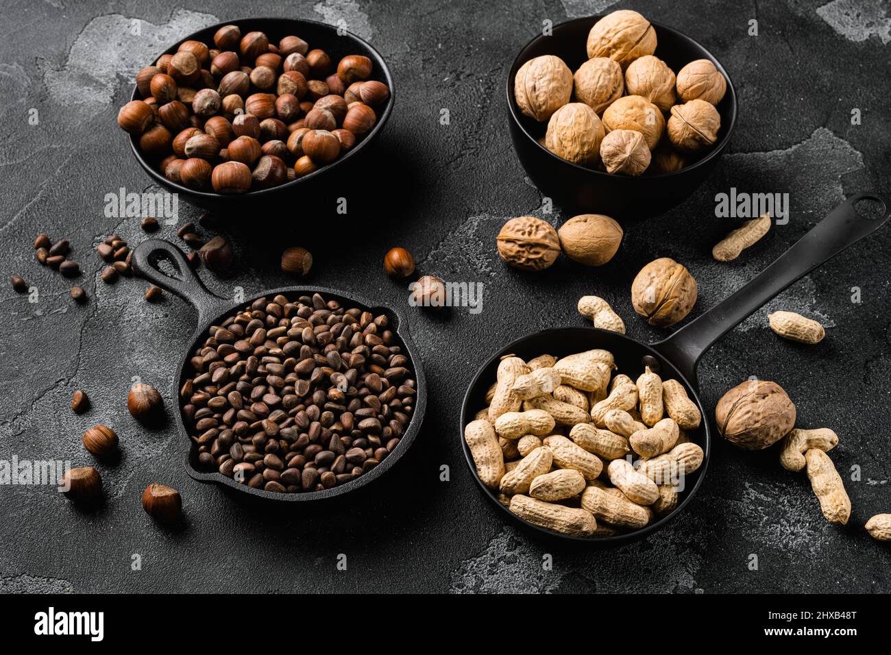 Assortment of nuts in shells, peanut, walnut, pine nuts and hazelnut set, on black dark stone table background Stock Photo