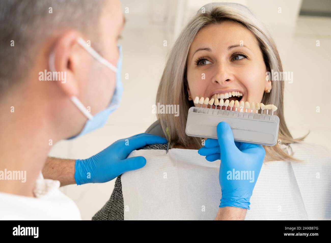 Dentist checks color on patient's teeth color chart before implantation procedure in dental