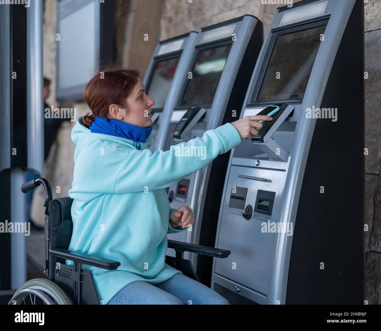 Caucasian woman in a wheelchair buys a train ticket using a mobile