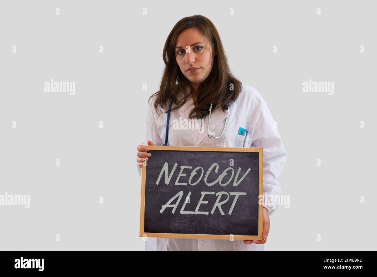 Serious female doctor holding blackboard with Neocov alert. New kind of coronavirus. Isolated on grey background. Stock Photo