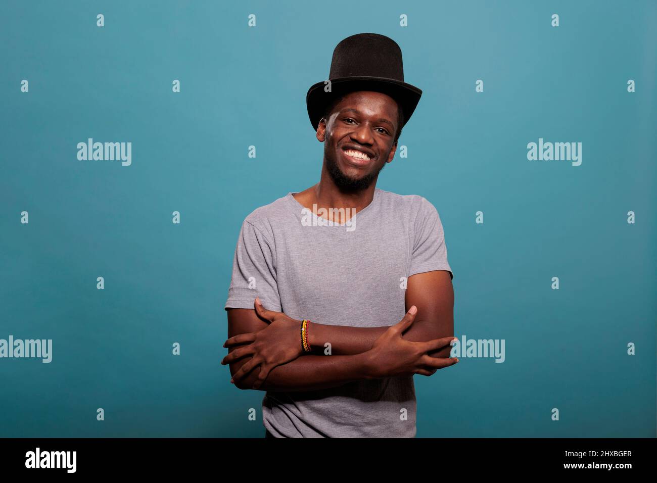 African american man with arms crossed wearing top hat to create magical artistic performance, showing confidence for vintage fashion. Young adult with theater prop costume in studio. Stock Photo