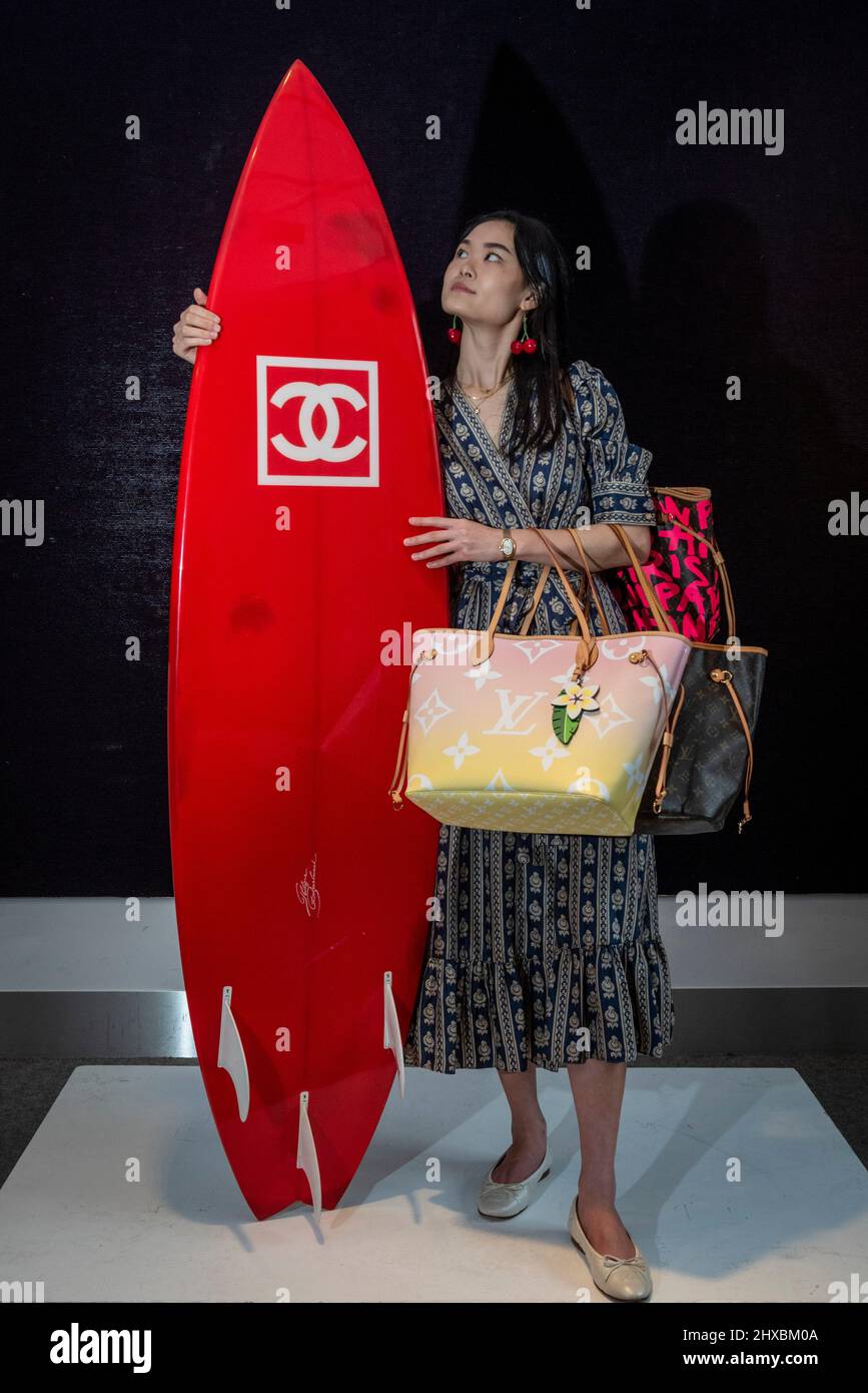 London, UK. 11 March 2022. A staff member presents a red carbon fibre Chanel  Surfboard with three keels (Est. £2,000 – 3,000) and a Louis Vuitton light  pink Monogram Giant 'By the
