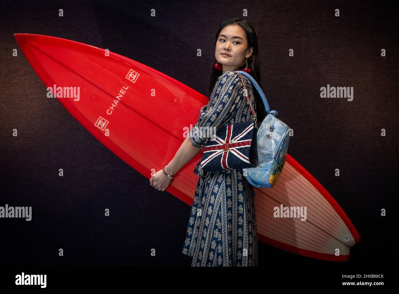 London, UK. 11 March 2022. A staff member presents a red carbon fibre Chanel  Surfboard with three keels (Est. £2,000 – 3,000) and a Chanel Union Jack  shoulder bag (Est. £2,000 –