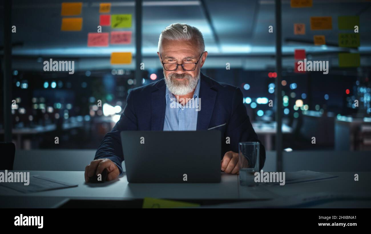 Successful Senior Businessman Working on Laptop Computer in Big City Office Late in the Evening. Investment Analyst Checking Financial Management Repo Stock Photo