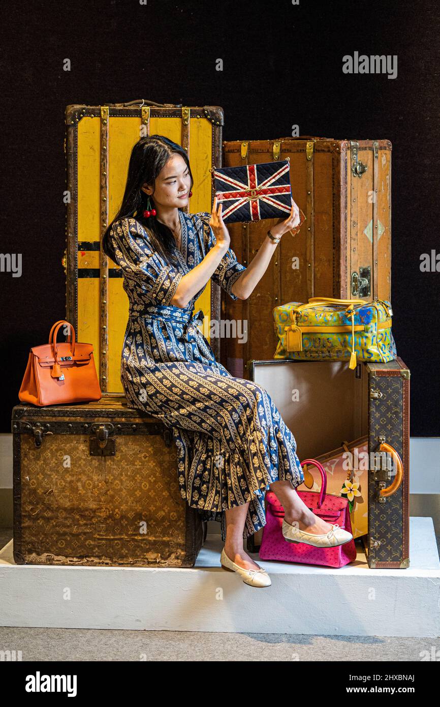 LONDON, 11 March, 2022 . A staff member presents a Union Jack shoulder bag, Estimate £2,000 – 3,000 alongside other luxury handbags with Louis Vuitton luggage which will be