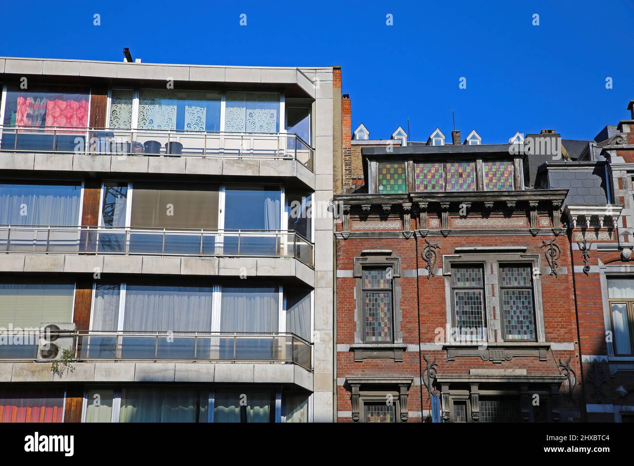 View on two facades side by side together with blue sky. Modern appartment building is neglected and in need of renovation, old medieval brick house i Stock Photo