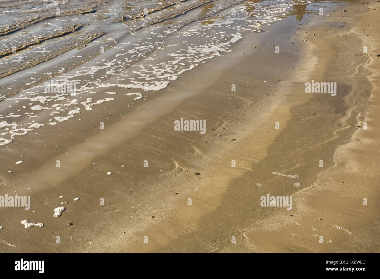Tiny waves and foam on sandy beach. Littlehampton, West Sussex, England Stock Photo