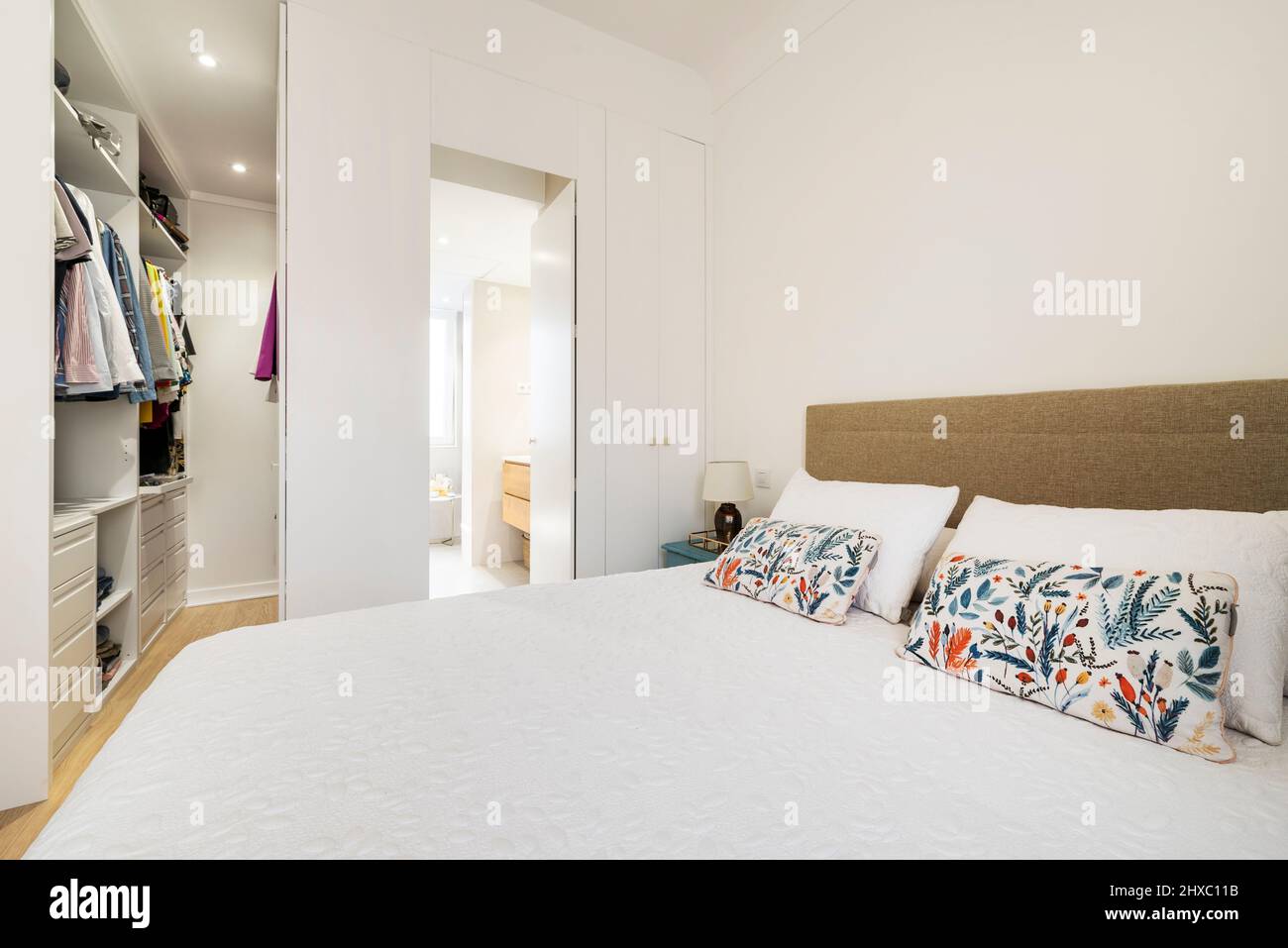 King size bed with flowery cushions in bedroom with dressing room and en-suite bathroom Stock Photo