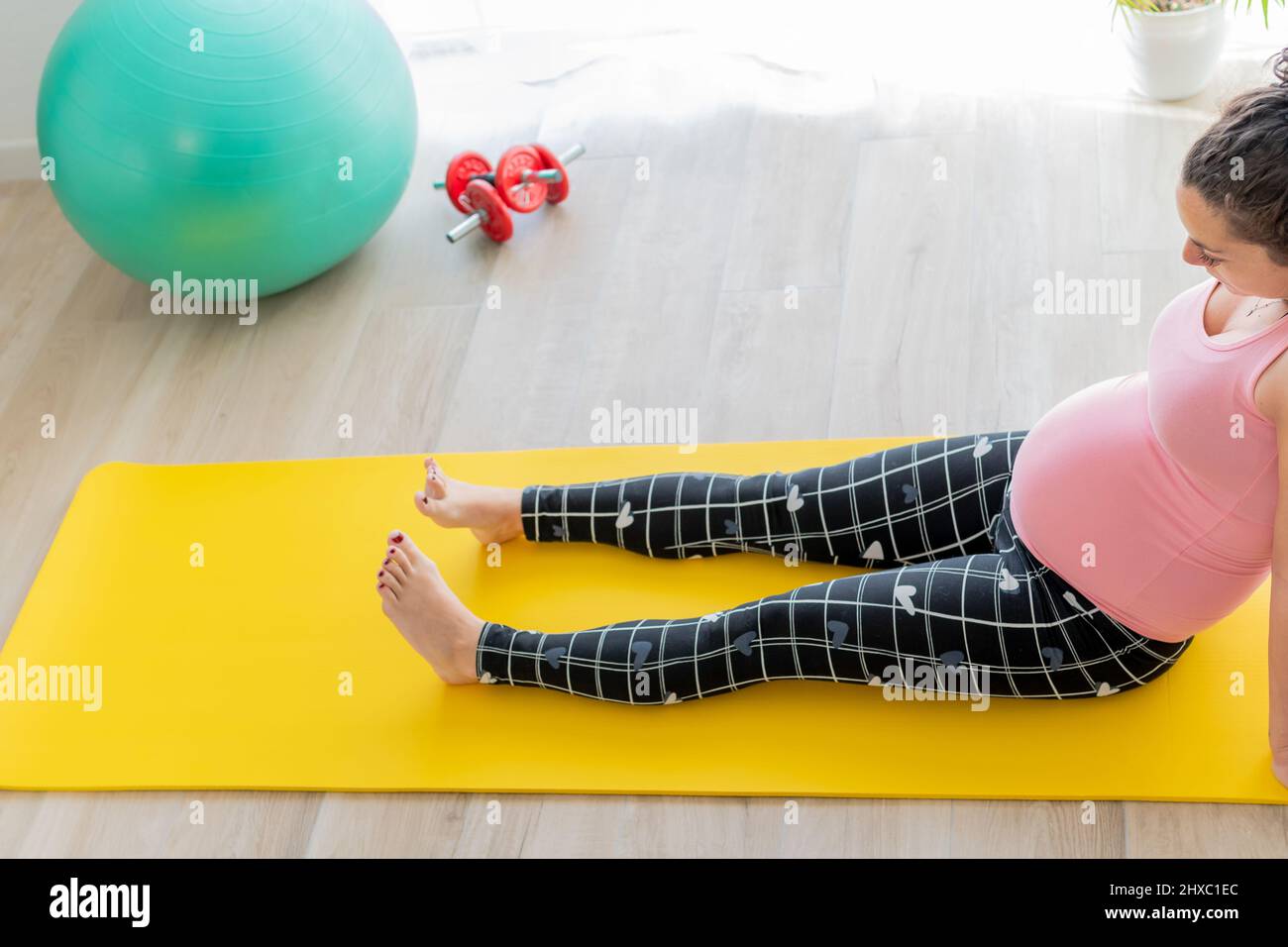 young pregnant woman sitting on the floor on an exercise mat does