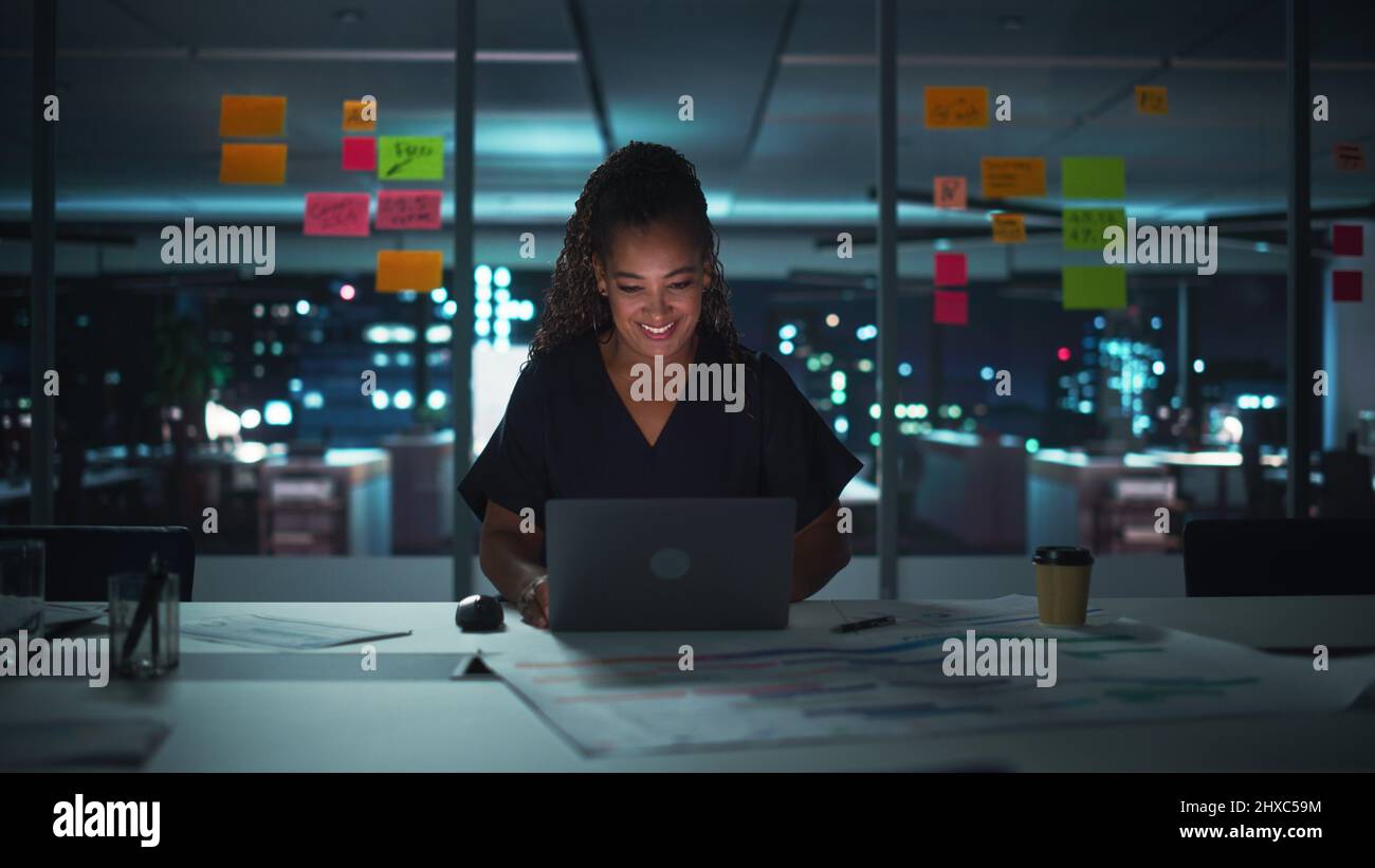 Successful African American Businesswoman Working on Laptop Computer in Big City Office Late in the Evening. Female Executive Director Managing Digita Stock Photo