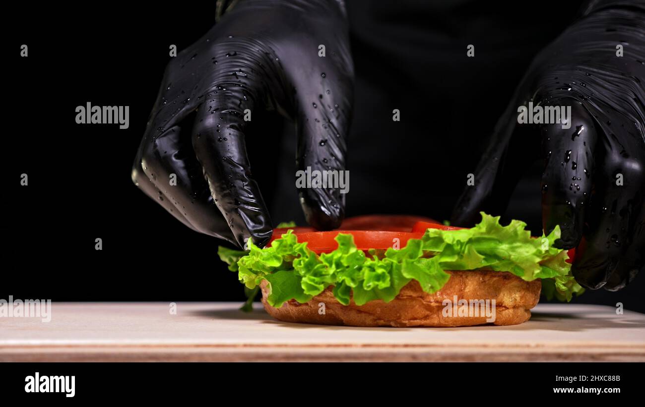 Craft burger is cooking on black background in black food gloves ...