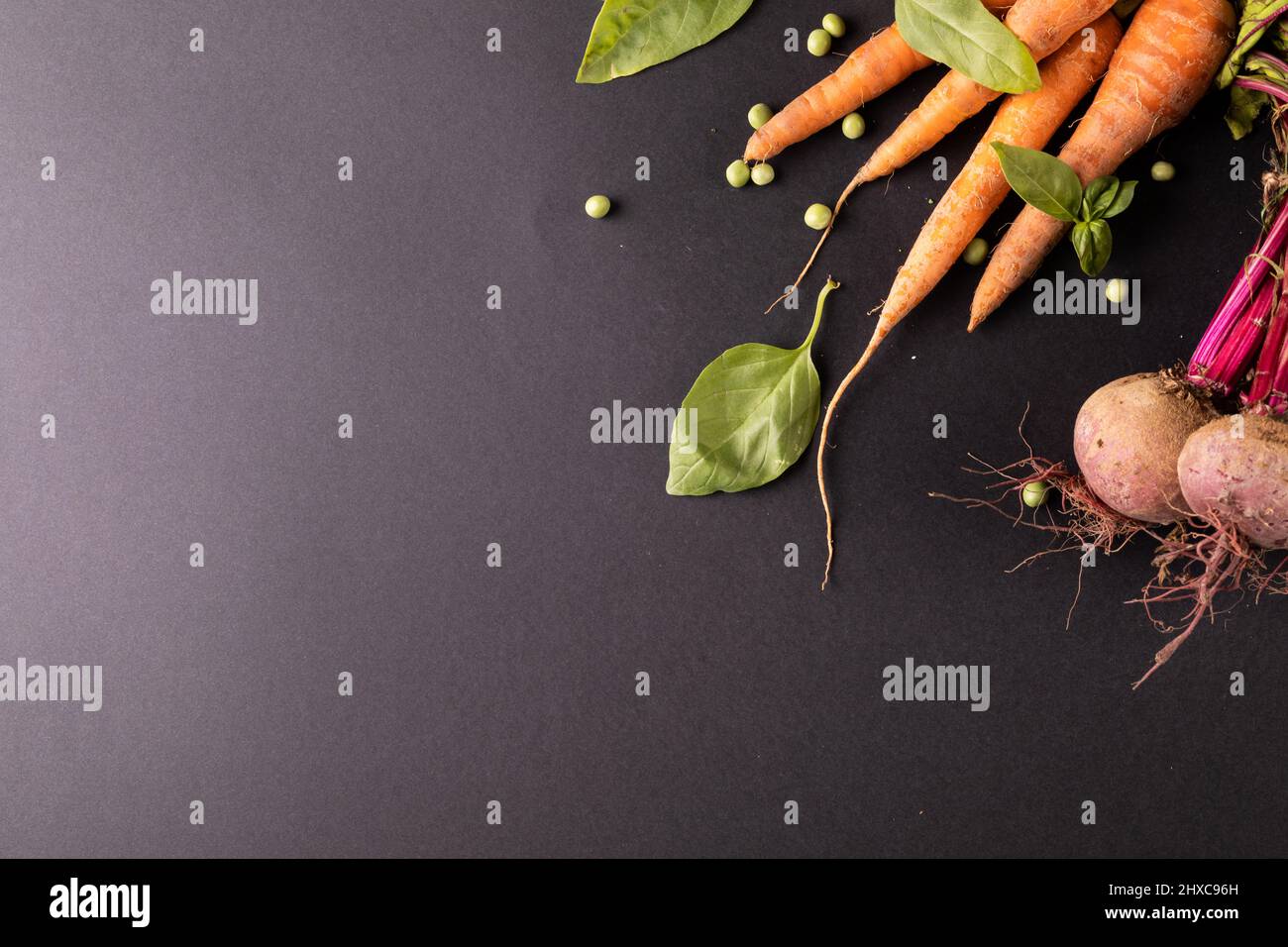 High angle view of carrots and beetroots with green peas and leaf vegetable on black background Stock Photo