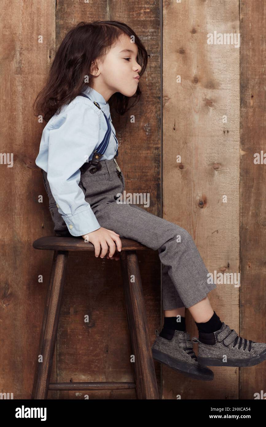 I like my style old-school. Shot of a cute little boy in old-fashioned overalls sitting on a stool. Stock Photo