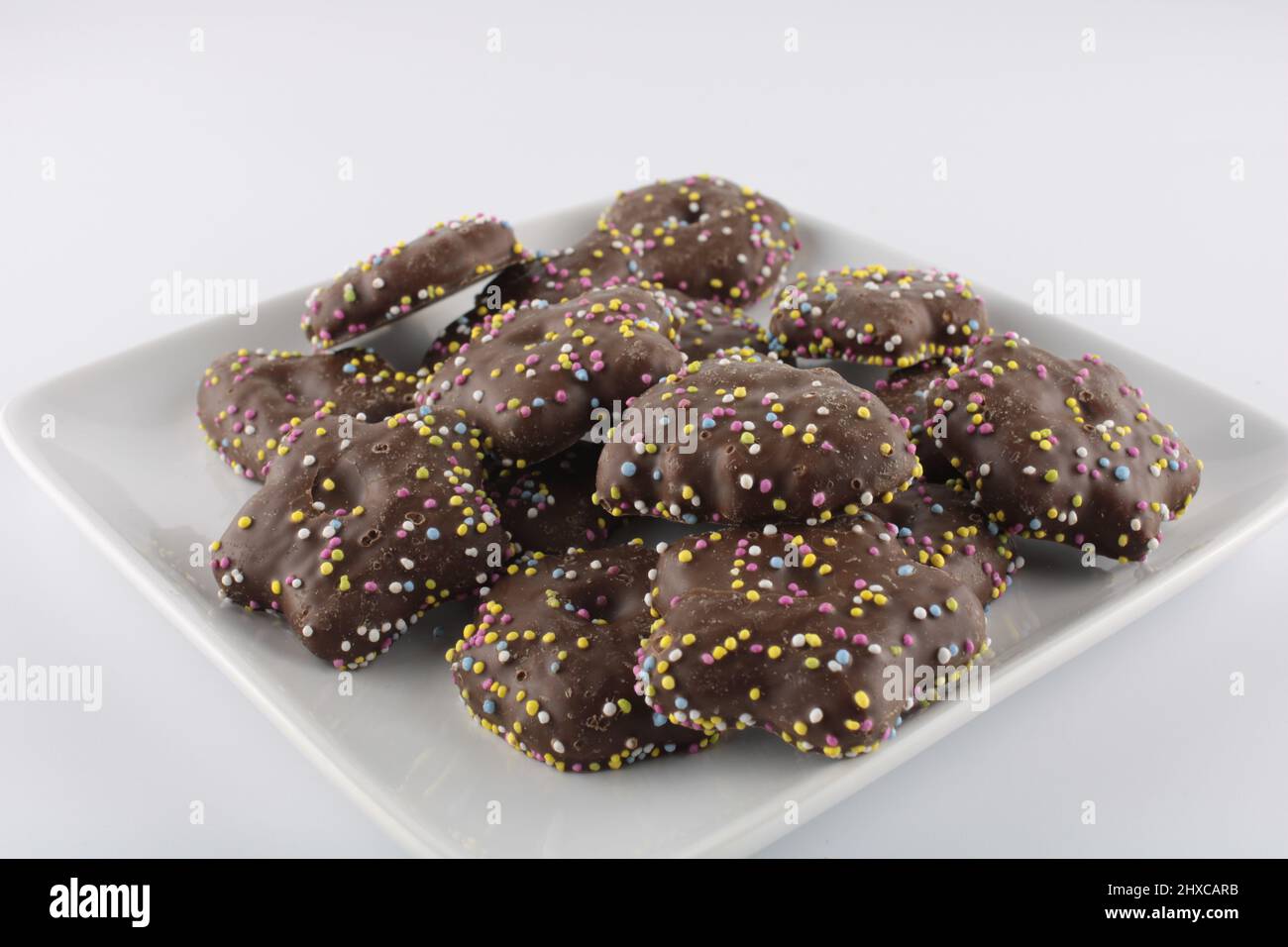 Biscuits covered in chocolate with hundred and thousands sprinkles isolated on a plate with copy space.  Sweet treats concept Stock Photo