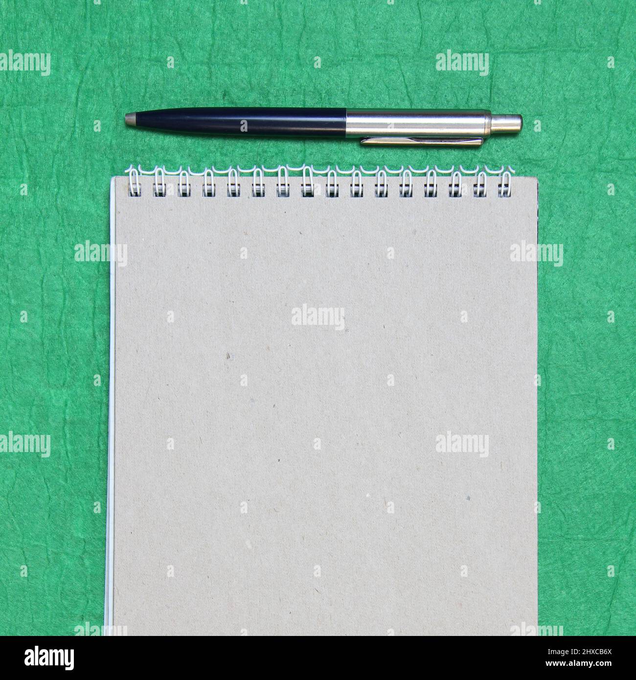 White and gray notepad sheet with spiral with pen against the background of green fabric. Concept of analysis, study, attentive work. Stock photo with empty place for your text and design. Square image shape. Stock Photo