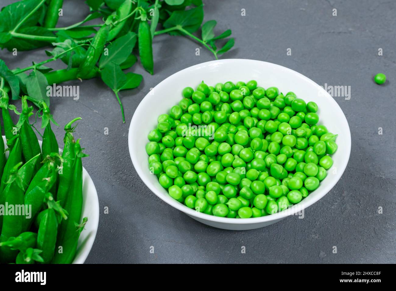 Healthy food. Fresh green peas in a white bowl with leaves and sweet pea pods on a gray background Stock Photo