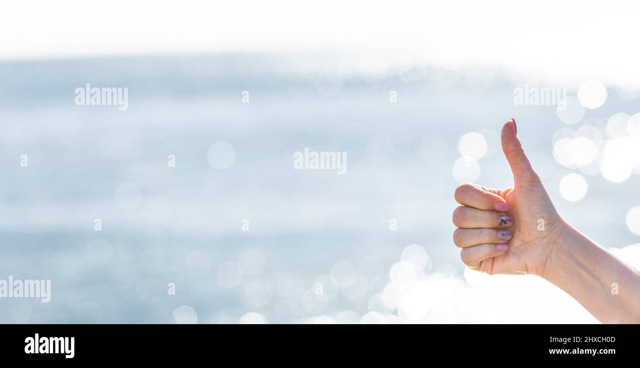 Thumbs up in front of sparkling sea water Stock Photo