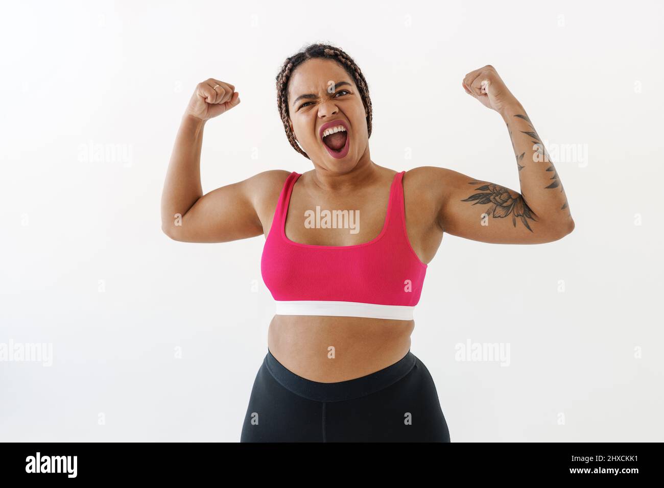 Excited young african bodypositive fitness woman over white wall background flexing biceps Stock Photo