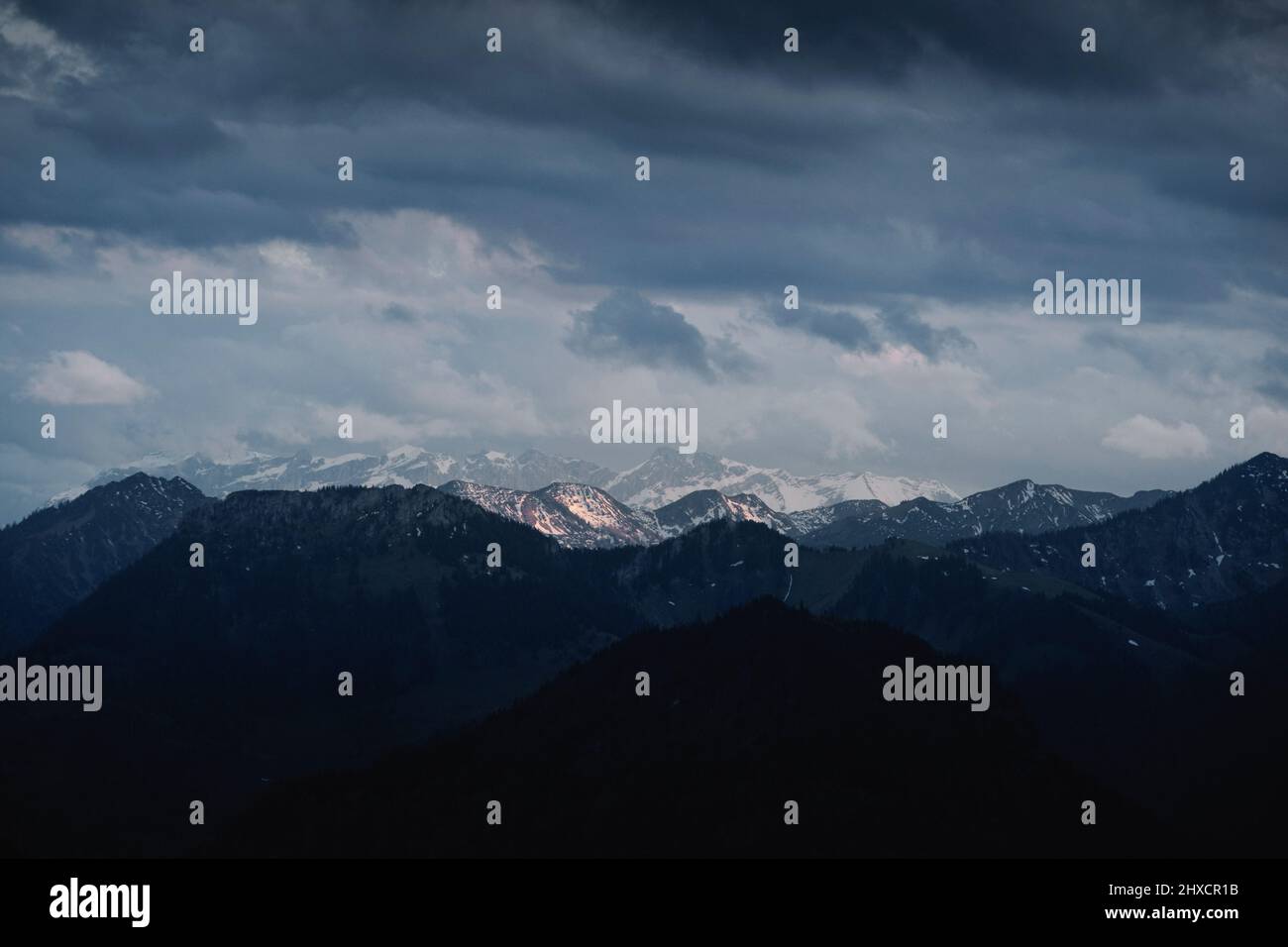 Landcsape image of distant mountains with peaks partly covered in snow under cloudy conditions during sunset Stock Photo