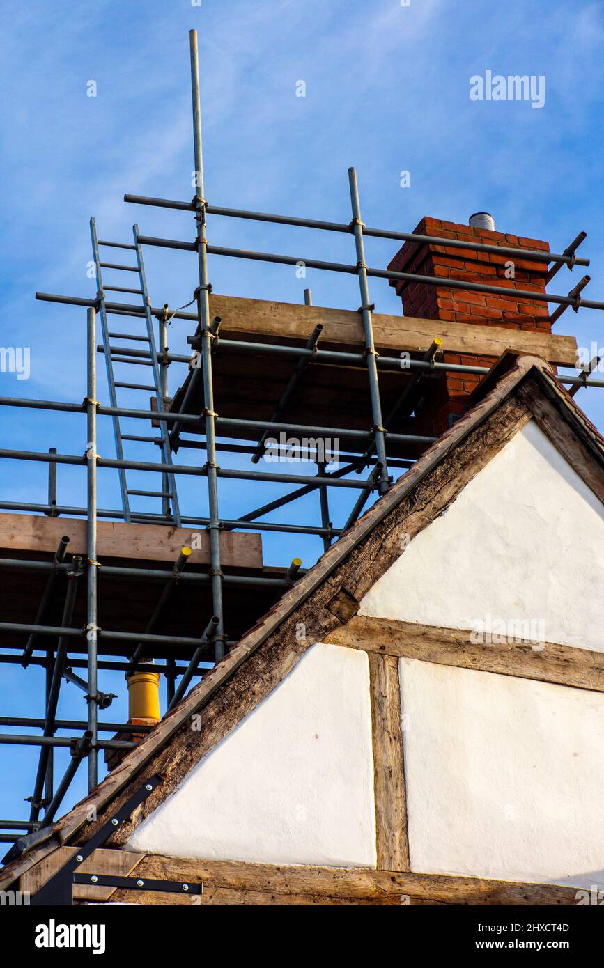 Ladders and scaffolding on the roof of a traditional medieval half timbered building with repair work taking place in England UK. Stock Photo