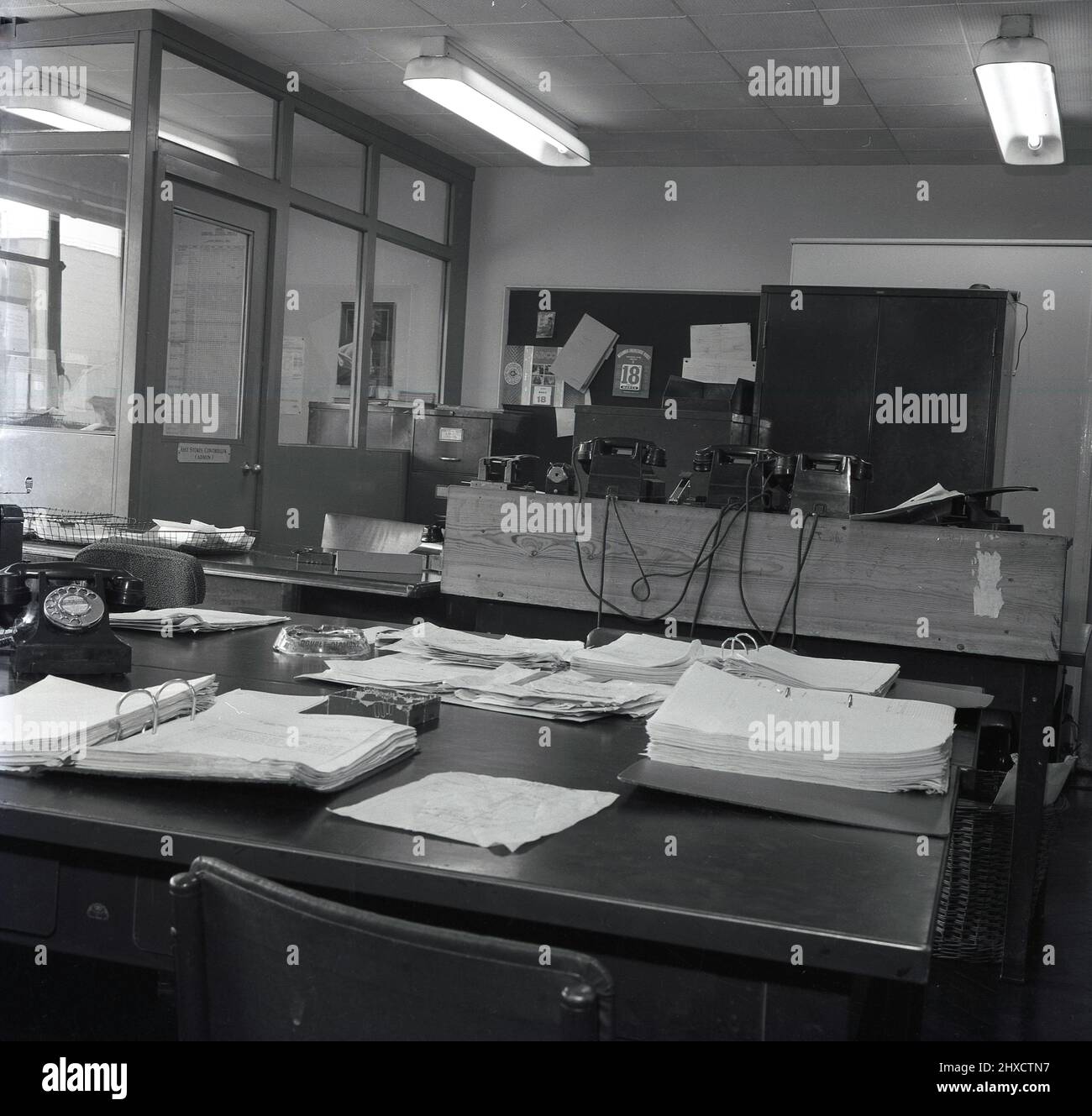1958, historical, view of an empty admin office an industrial premises, showing a paperwork, delivery notes and files on a desk, several dial-up bakerlite telephones of the era, and metal filing cabinets. A Double Diamond branded ashtray sits on the desk, Port Talbot, Wales, UK. Stock Photo