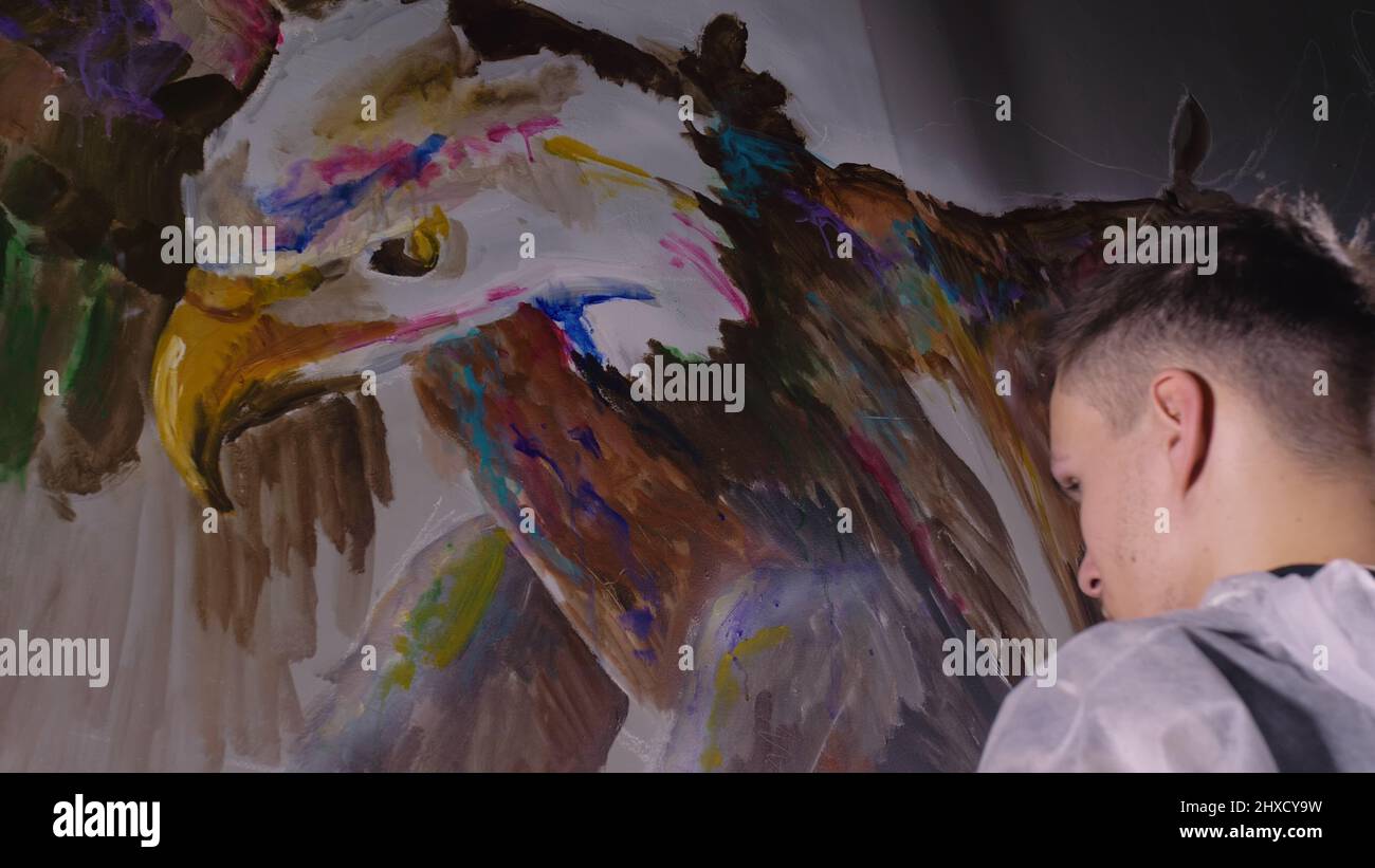 Artist designer draws an eagle on the wall. Craftsman decorator paints a picture with acrylic oil color. Painter painter dressed in a paint coat. Indo Stock Photo