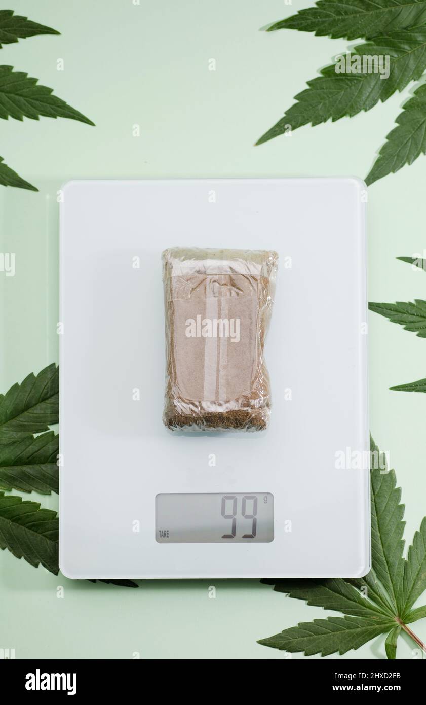 https://c8.alamy.com/comp/2HXD2FB/packaged-hashish-tablet-on-weight-scale-marijuana-leaves-green-background-2HXD2FB.jpg