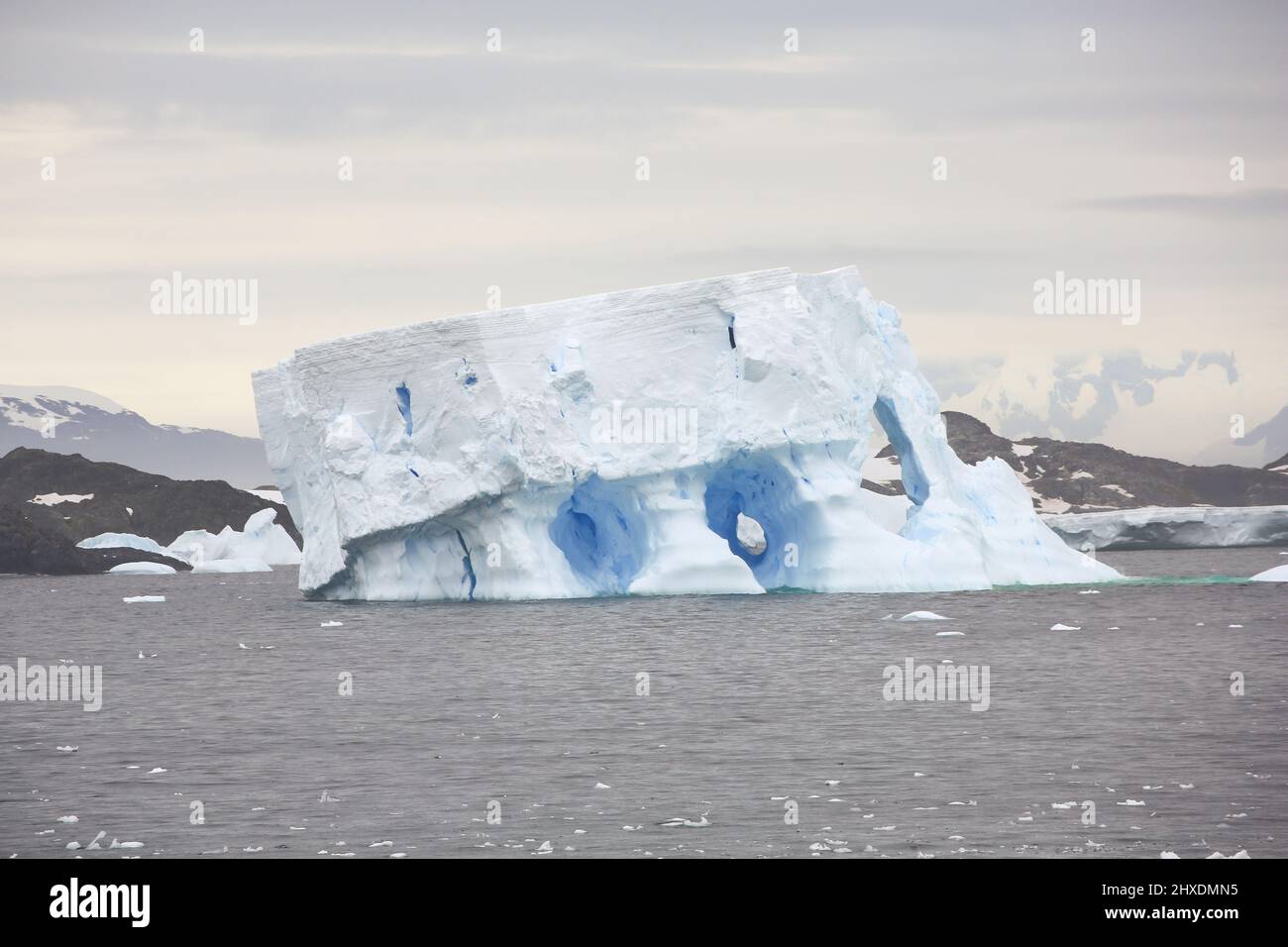 A large iceberg in the Wilhelm Archipelago region of the Antarctic Peninsula. Several caverns and holes have developed through the iceberg. Stock Photo