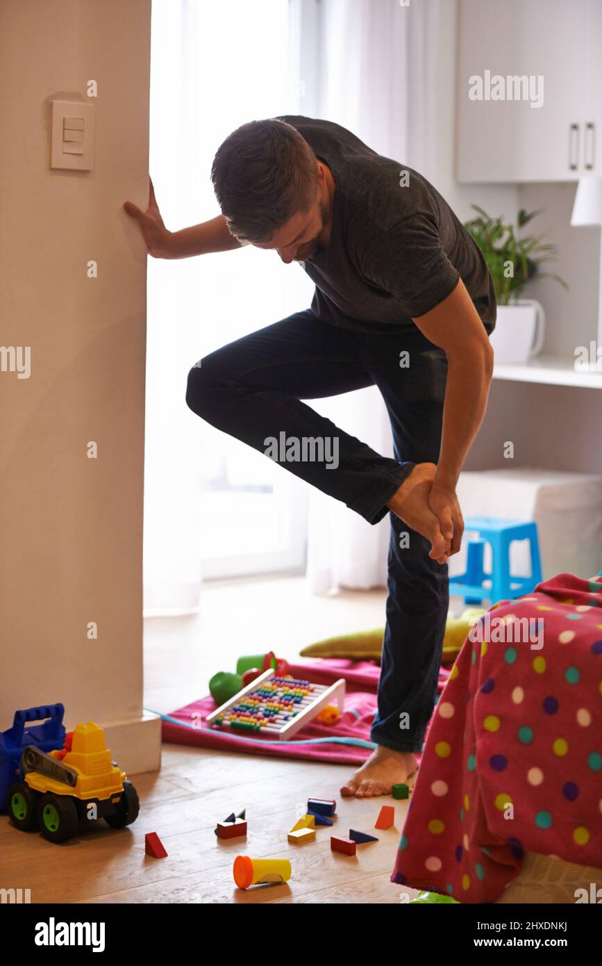 Ow I really hate it when that happens.... Shot of a man grabbing his foot in pain after standing on a childs toy. Stock Photo