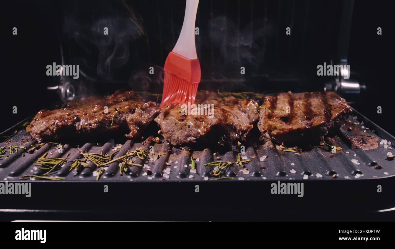 Delicious juicy meat steak cooking on grill. Silicone cooking brush