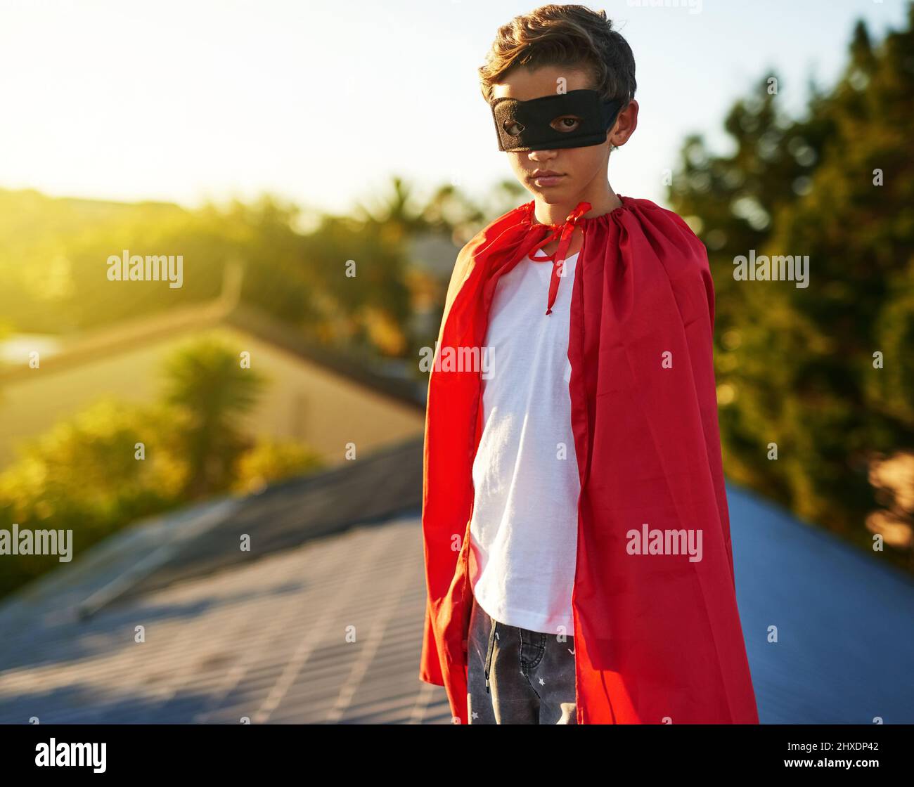 Watching over his neighbourhood. Portrait of a young boy in a cape and mask playing superhero outside. Stock Photo