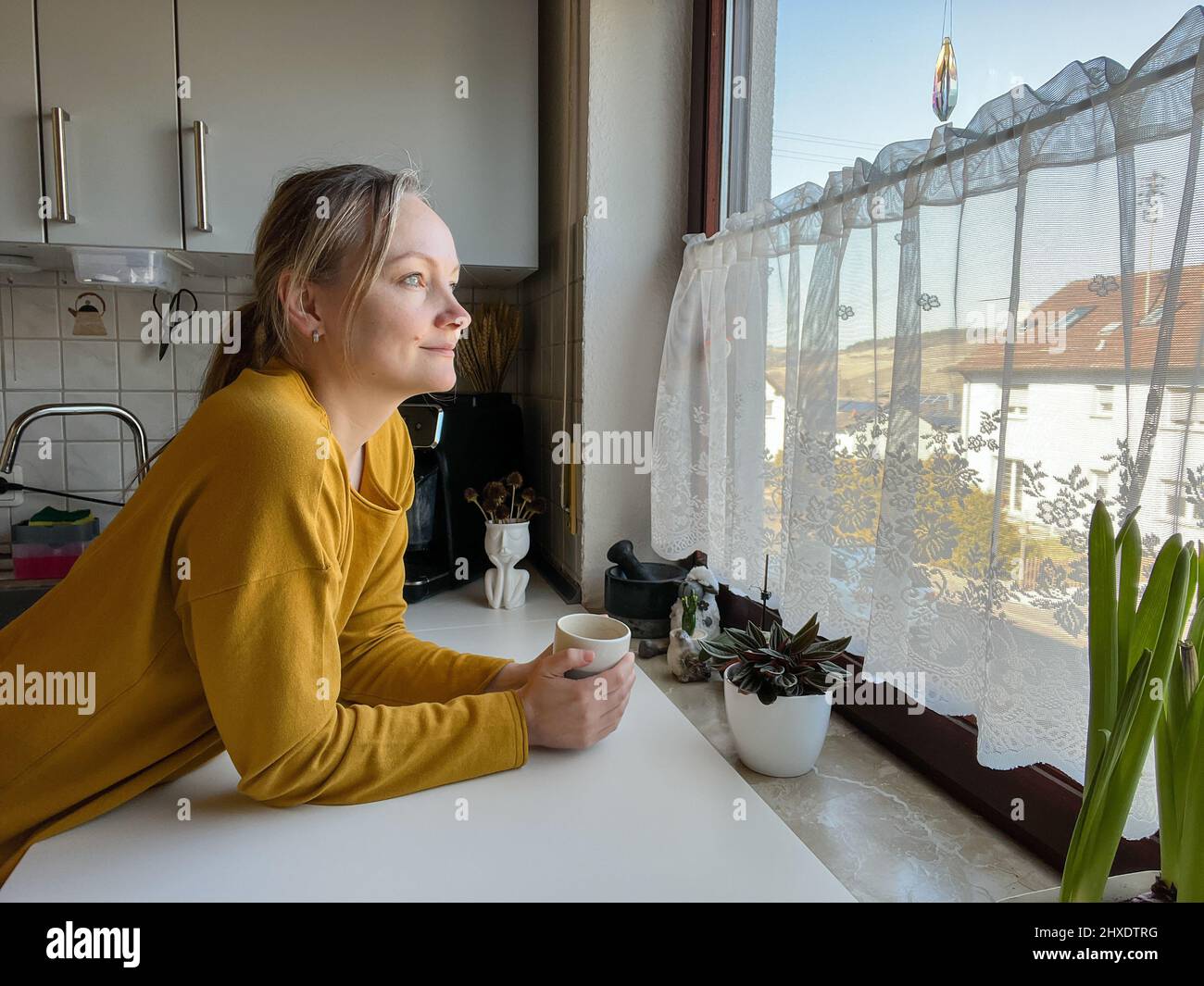 Woman is holding a cup whilst watching out of the window Stock Photo