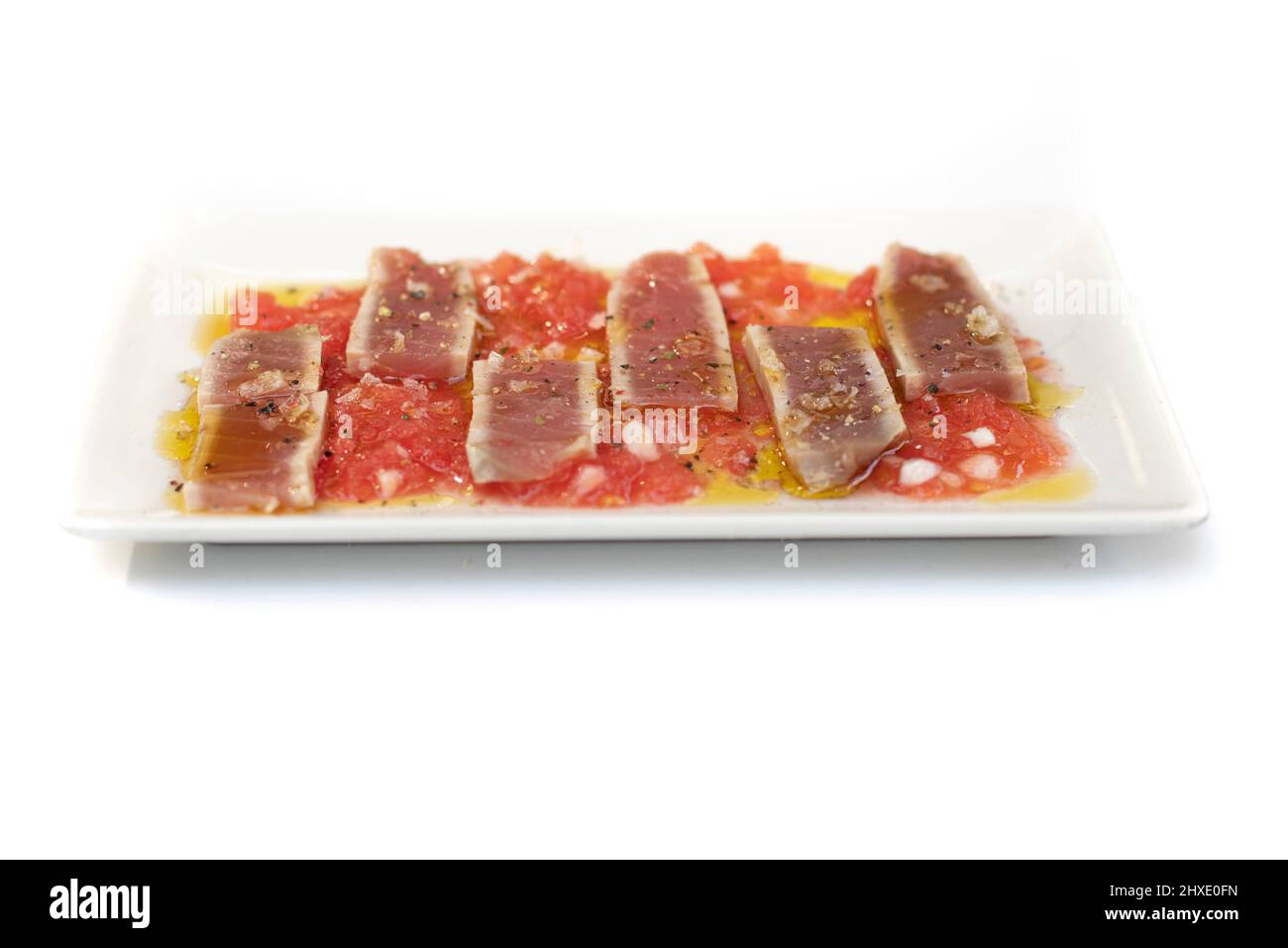 Plate with laminated red tuna, on minced fresh onion, grated tomato, flake salt and olive oil. Isolated on white background. Stock Photo