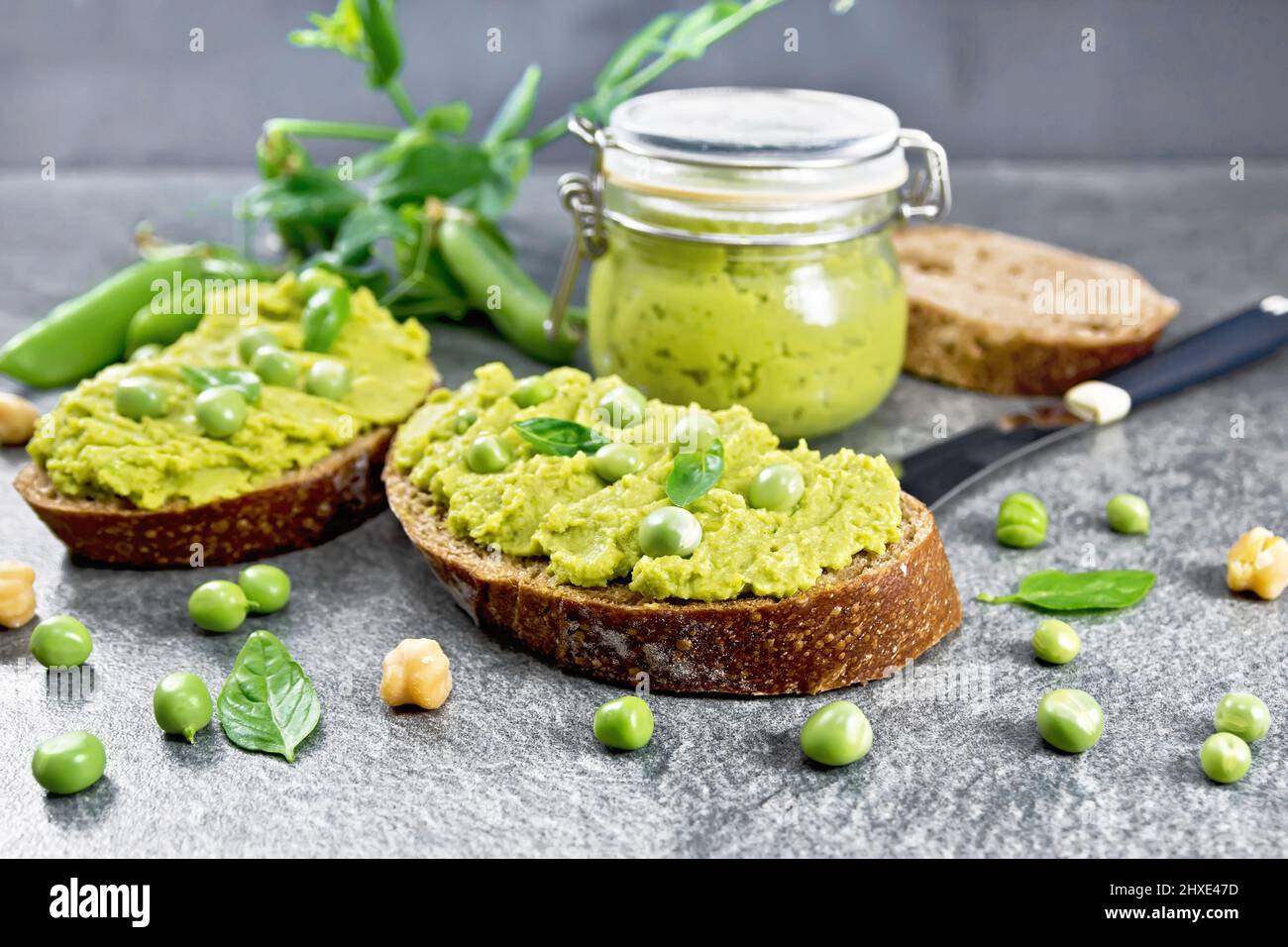 Green pea and chickpea hummus sandwiches, jar of dipping sauce, pea pods on granite countertop background Stock Photo