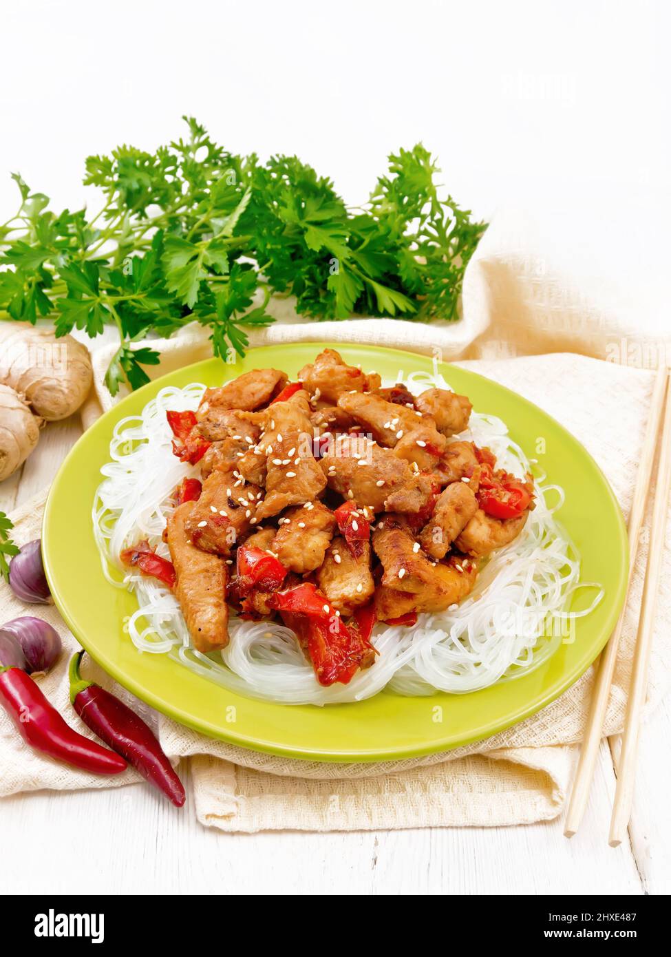 Stir-fry chicken with pepper, garlic, ginger and soy sauce, sprinkled with sesame seeds in a plate, napkin and parsley on a wooden board background Stock Photo