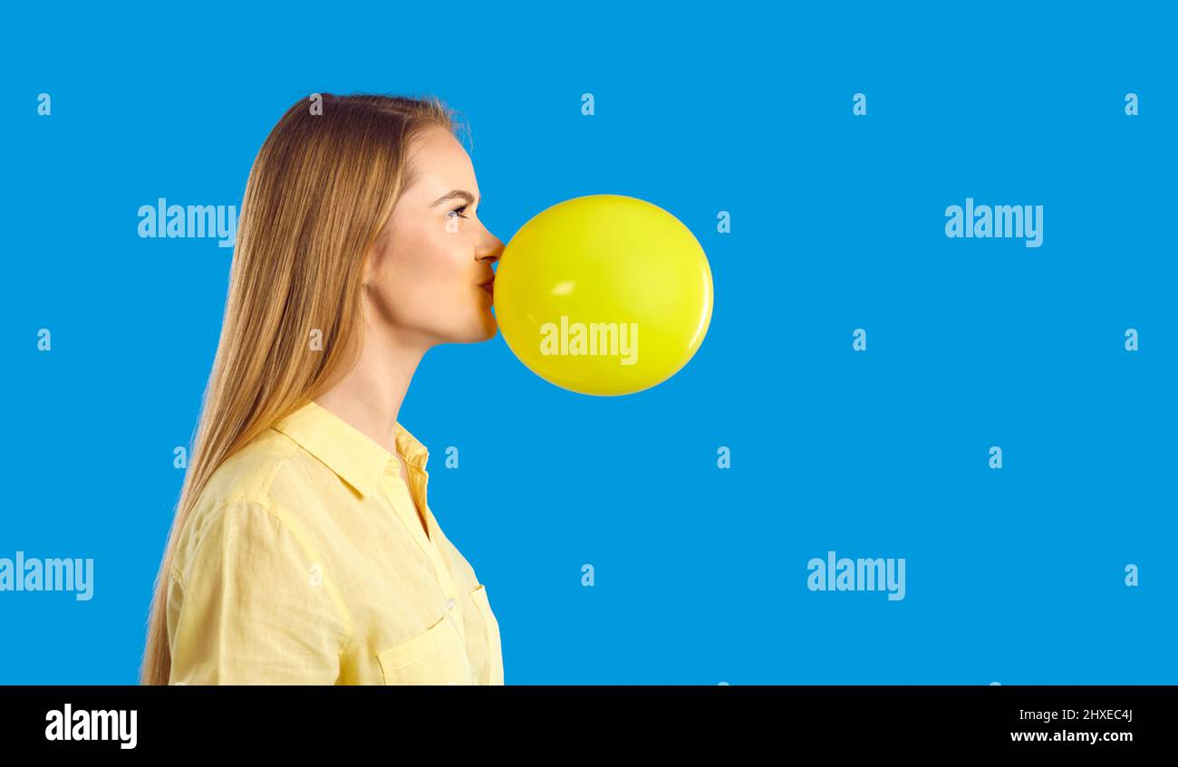 Side view of a happy young girl blowing up a yellow balloon isolated on a blue background Stock Photo