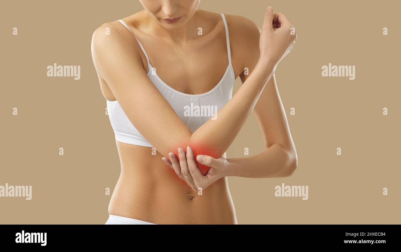 Young woman who suffers from elbow arthritis touches the area of pain on her arm Stock Photo